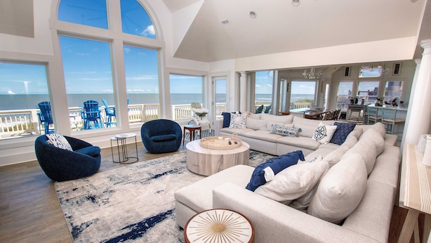 A spacious living room with a large window overlooking the sea, a cozy seating area with a sofa and armchairs, and a dining area with a view. - LUXURY, OCEANFRONT, Pool, ELEV, Rec Rm, Beach Access, Ocean Views! WL983, Fairlight (Corolla)