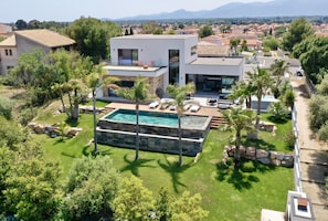 Une maison moderne dotée d’une piscine, entourée d’une végétation luxuriante et de palmiers.