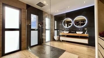 Une salle de bain moderne avec une douche à parois de verre, un grand miroir doté de lumières disposées en cercle et un meuble-lavabo en bois.