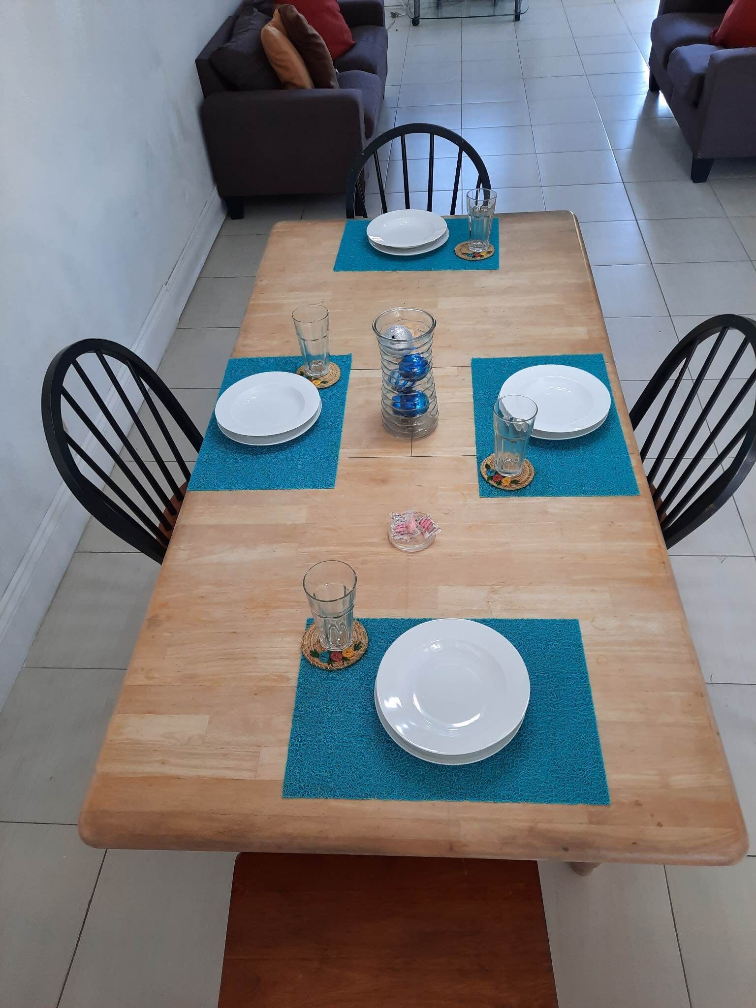 A dining table with chairs, plates, glasses, and a decorative glass vase.