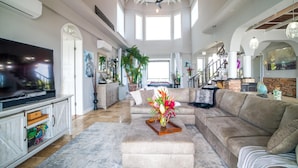 Ein geräumiges Wohnzimmer mit einem großen Flachbildfernseher, einem beigen Sofa und einem Couchtisch mit Blumenarrangement.
