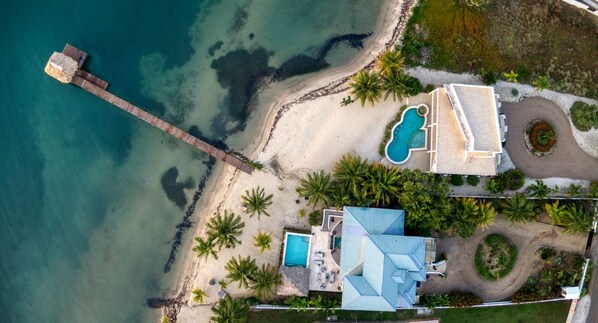 Una propiedad costera con playa, piscina y una casa grande de techo azul.