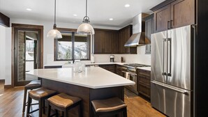 A modern kitchen with dark wood cabinets, stainless steel appliances, and a large island with stools. - The Sunrise Ridge Chalet (Whitefish)