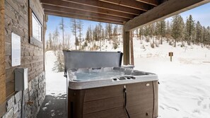 A hot tub in a wooden cabin with a snowy outdoor view. - The Sunrise Ridge Chalet (Whitefish)