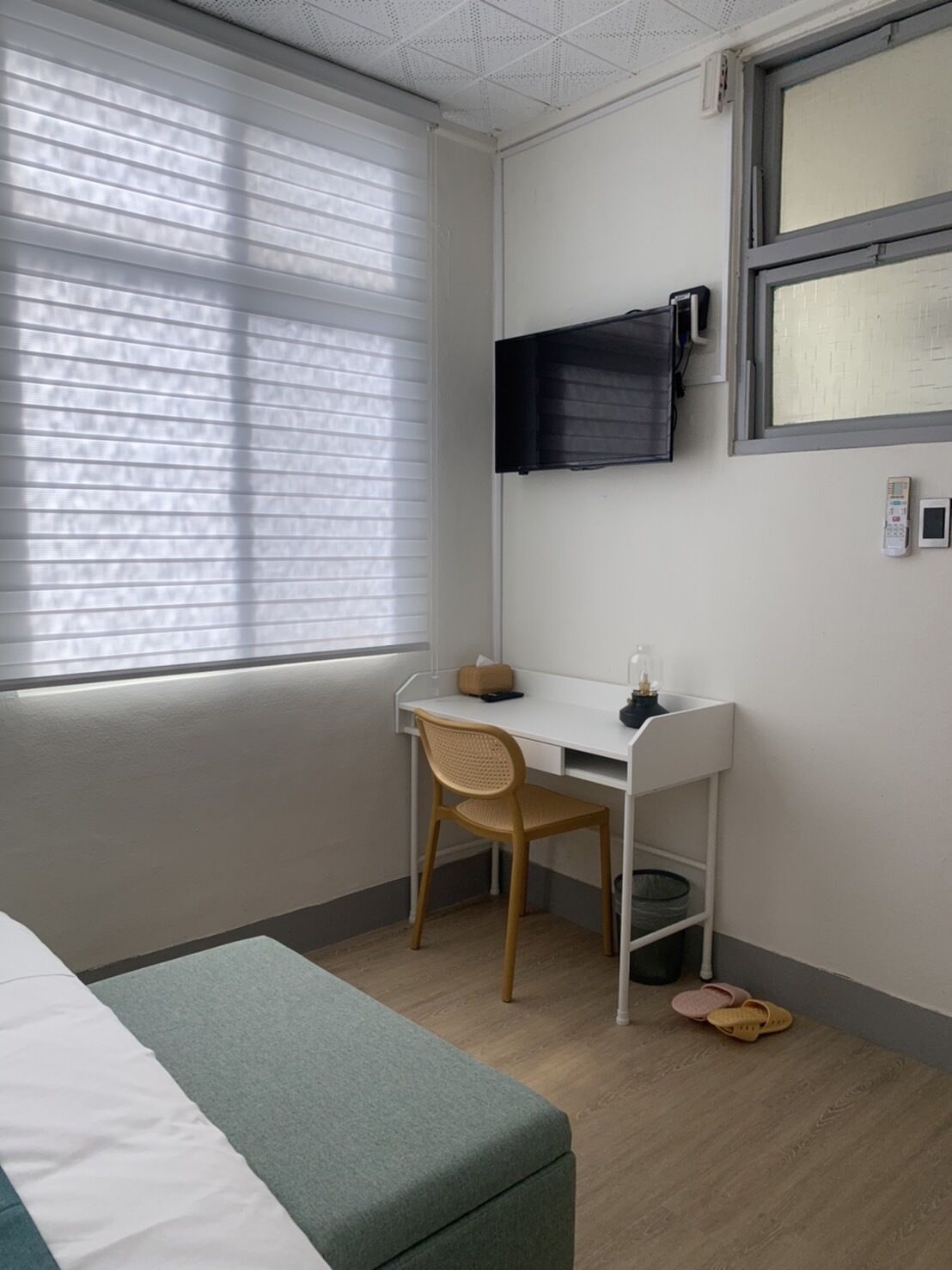 A hotel room with a bed, a desk, a chair, a television, and a window with blinds.