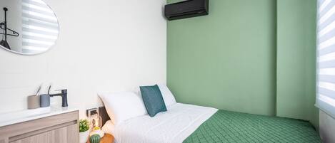 A bedroom with a green wall, a white bed, a round mirror, a bedside table with a lamp, and a small plant.