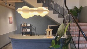 A reception desk with a modern design, a staircase with decorative railings, and a potted plant.