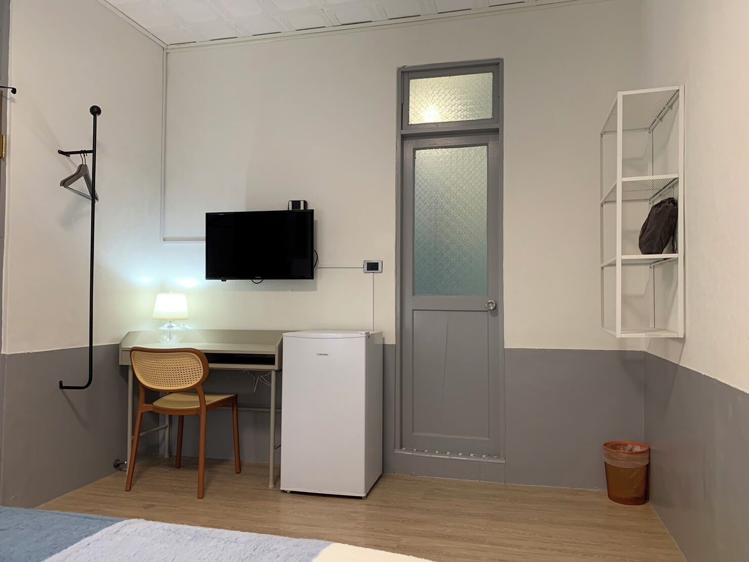 A compact room with a desk, chair, television, and a door with a frosted glass panel.