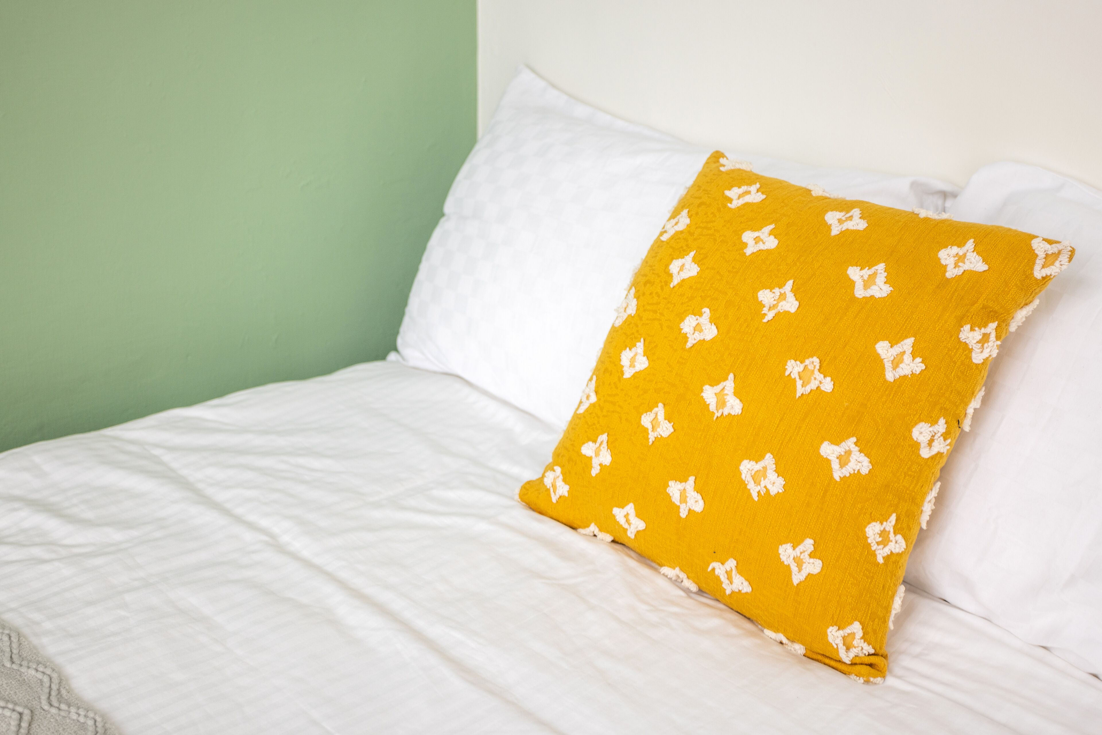 A bed with white bedding and a single yellow pillow with white patterns.