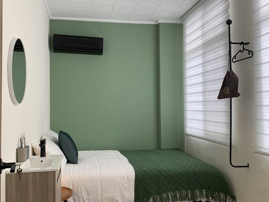 A bedroom with a bed, a ceiling fan, a window with blinds, a bedside table, and a hanging light fixture.