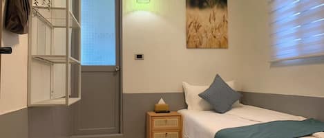 Un dormitorio con cama, mesita de noche, estante en la pared, ventana y un cuadro.