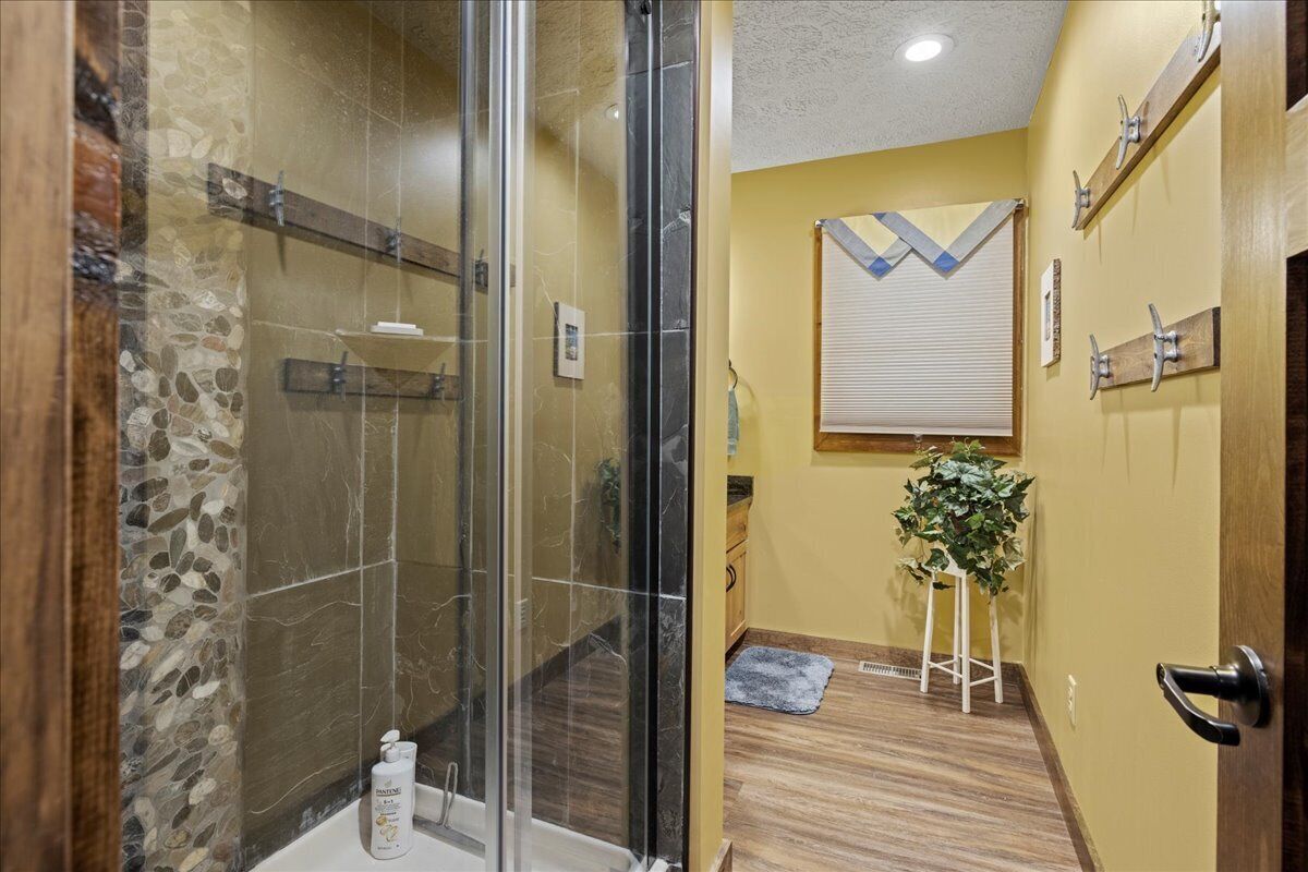 A bathroom with a glass-enclosed shower, a wooden vanity, and a potted plant.