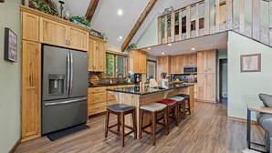 Een ruime keuken met houten kastjes, een groot eiland met barstoelen en een entresol.