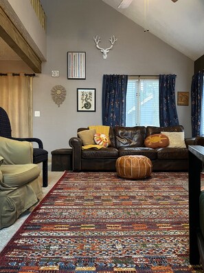 A living room with a brown leather sofa, a patterned rug, and a deer skull wall decoration.