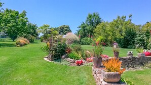 Un jardín bien cuidado con diversas plantas y flores, un muro de piedra y un cielo azul despejado.