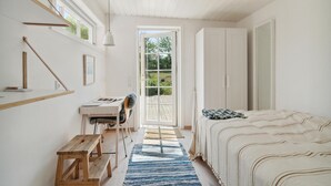 Un dormitorio con una cama, un escritorio y una silla. Hay una ventana y una puerta que da al exterior.