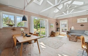 Una habitación amplia con piso de madera, una mesa de comedor con sillas, un sofá y un ventanal con vista a zonas verdes.