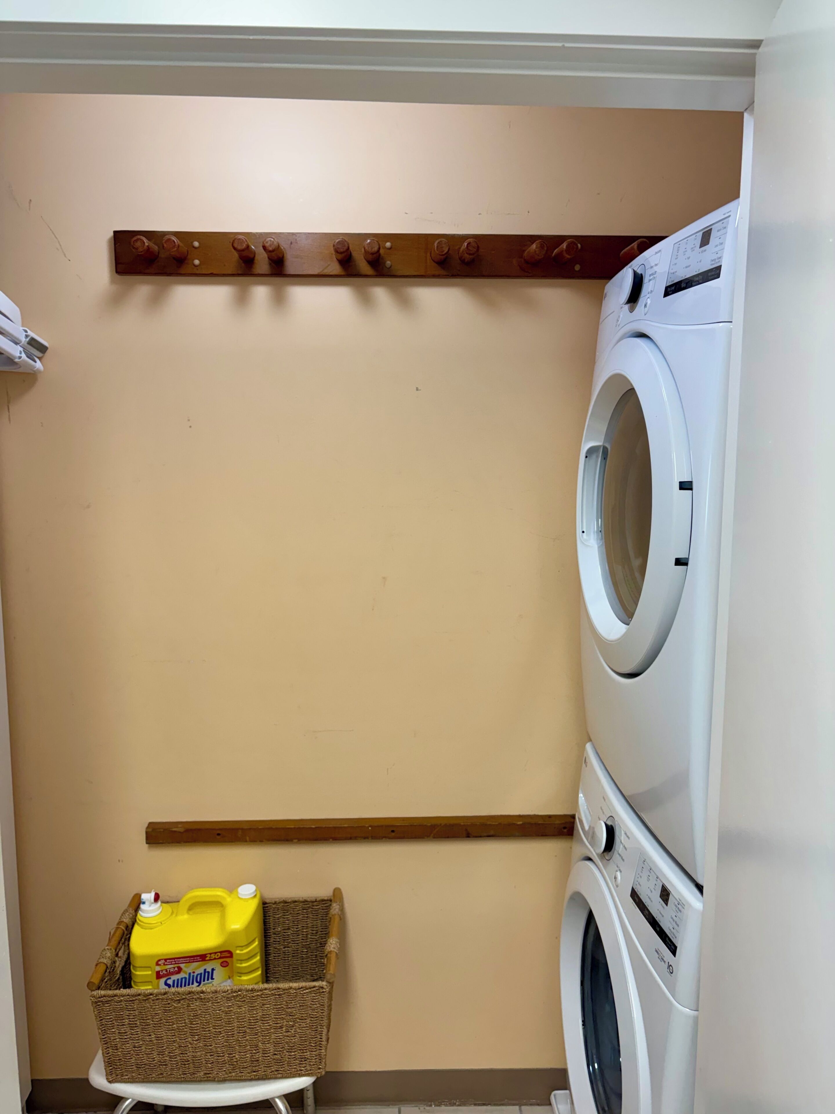 Une buanderie équipée d’un lave-linge et d’un sèche-linge superposés, d’une étagère avec des bouteilles et d’un panier contenant de la lessive.