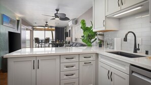 A modern kitchen with white cabinetry, a large island, and a dining area with a view. - Direct Ocean Front Luxury Condo (Kailua-Kona)