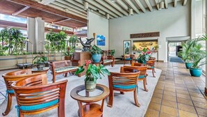 A spacious indoor area with wooden furniture and potted plants, featuring a high ceiling and a view of the outdoors. - Direct Ocean Front Luxury Condo (Kailua-Kona)