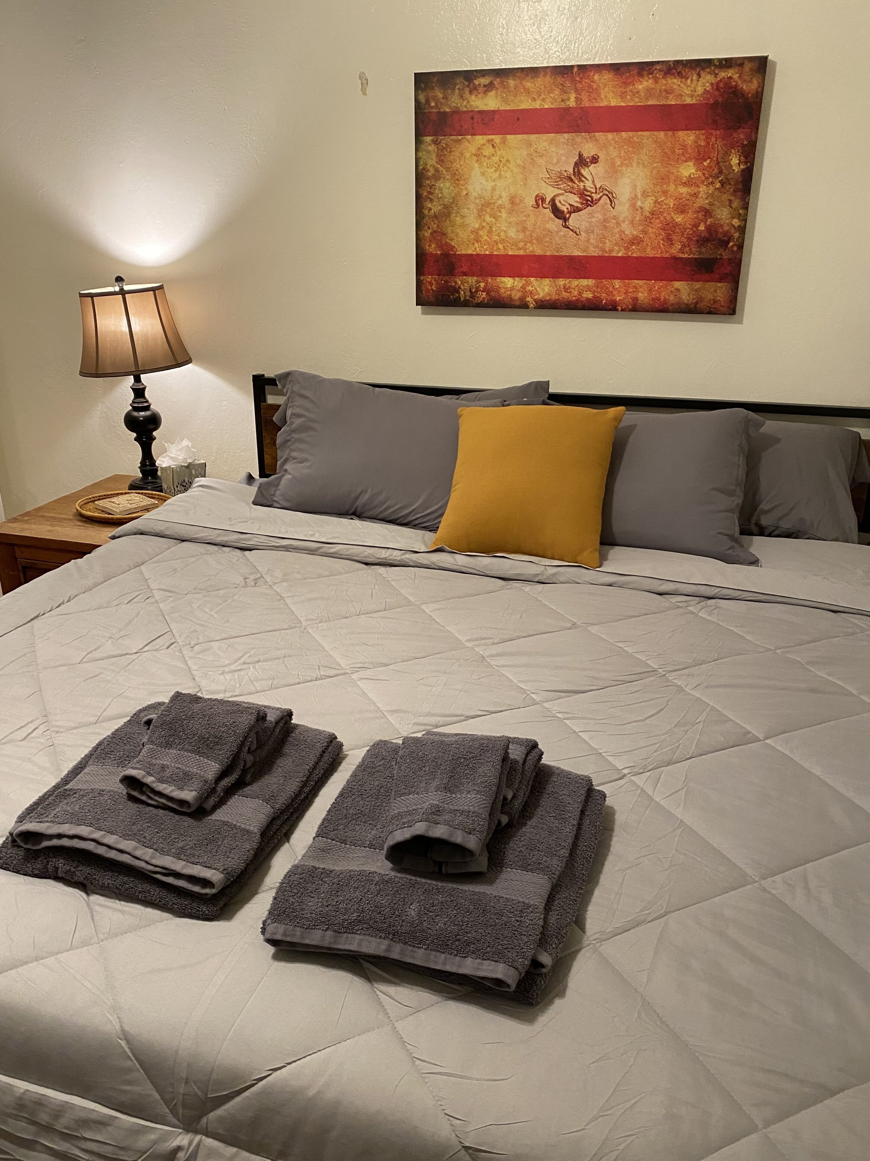 Un lit bien fait, avec une couvre-lit matelassé, deux serviettes pliées et une lampe sur une table de chevet.