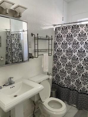 Baño con lavamanos, inodoro y cortina de ducha con estampado blanco y negro.
