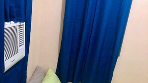 Ein kleines Bett mit einer grünen Decke, zwei Kissen und zwei zusammengerollten Handtüchern. An der Wand befindet sich eine weiße Klimaanlage.