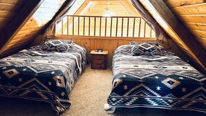 Een klein zolderkamer met twee bedden, een tafeltje en een raam met houten balustrade.
