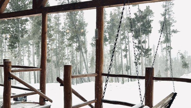 Een houten terras met een bank en tafel, omringd door een houten leuning, met uitzicht op een besneeuwd bos.