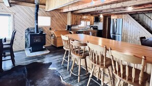Een rustiek houten interieur met een eethoek, een open haard en een keuken met houten kasten en een koelkast.