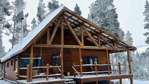Een houten hut met een overdekte veranda en een steil dak, omringd door met sneeuw bedekte bomen.