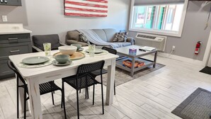 A modern living room with a dining area, a gray sofa, a coffee table, and a large American flag on the wall.