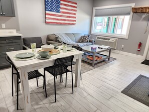 A modern living room with a dining area, a gray sofa, a coffee table, and a large American flag on the wall.