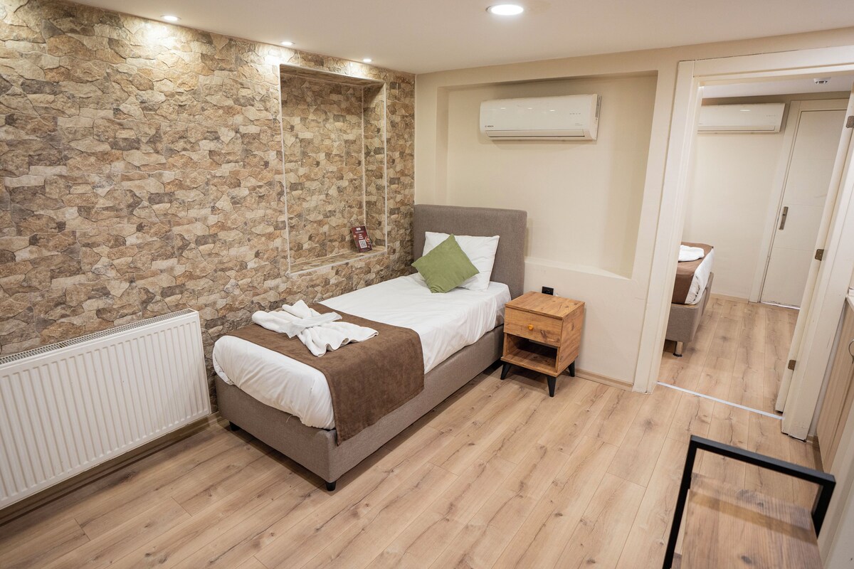 A bedroom with a stone wall, a bed with a green pillow, a wooden nightstand, and an air conditioning unit.