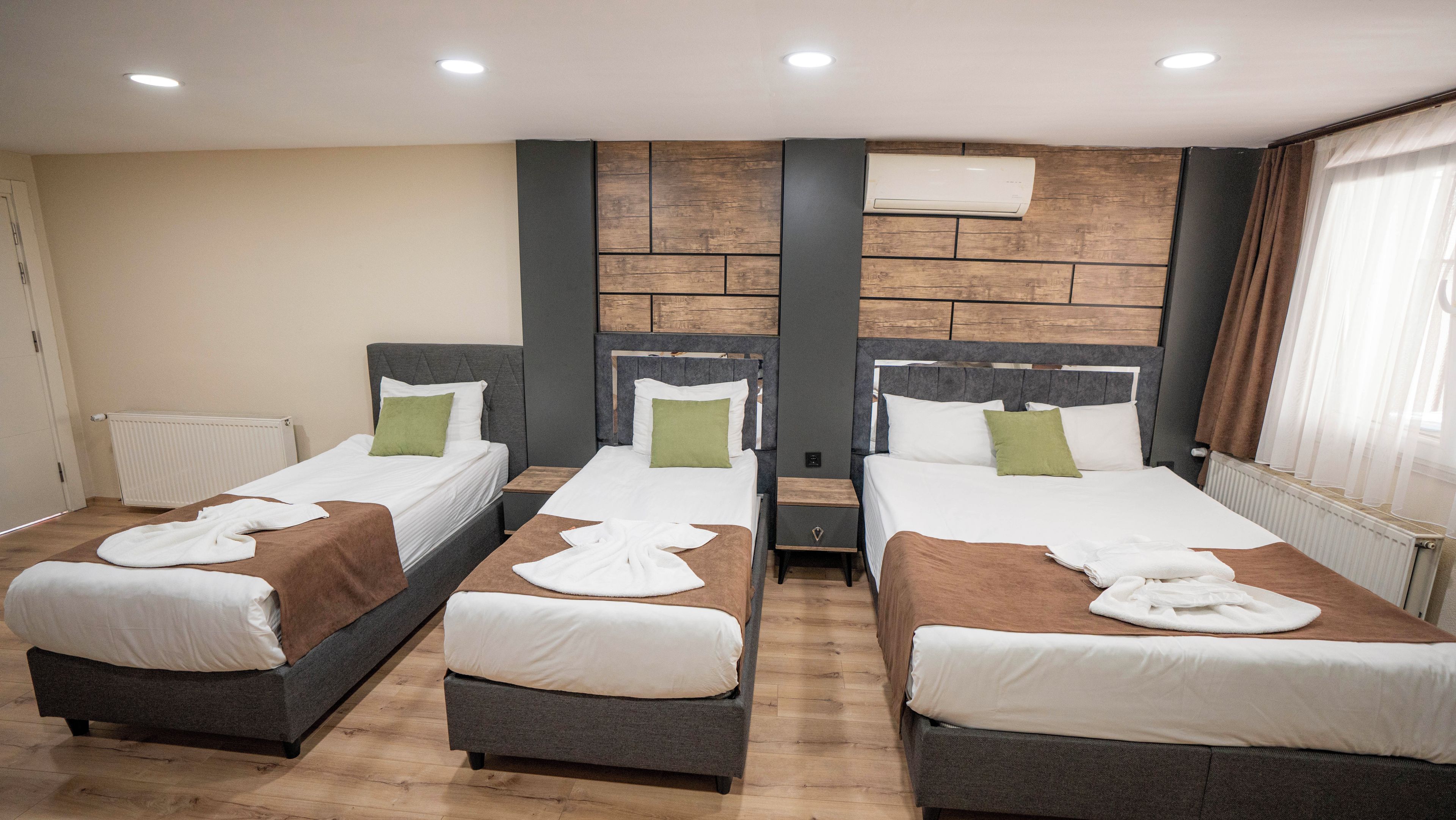 Une chambre d’hôtel avec deux lits, un mur décoratif en bois, un radiateur et une fenêtre avec des rideaux.