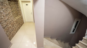 A hallway with a stone wall, a white door with a number plate, and a staircase with a window.