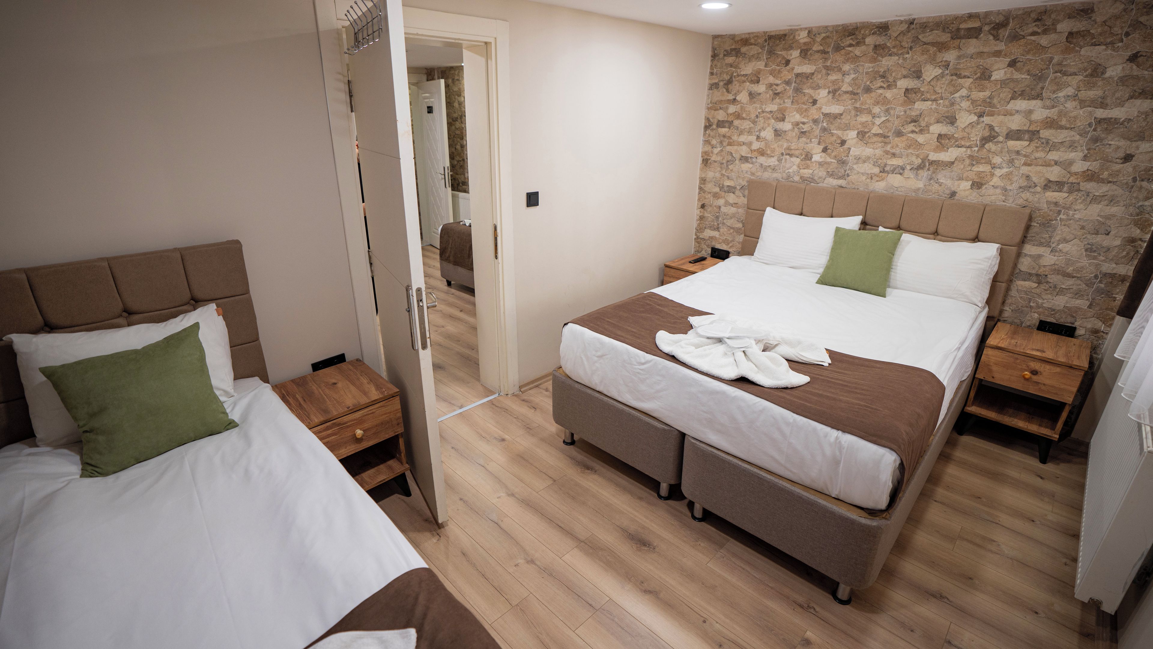 Ein Hotelzimmer mit zwei Betten, einer Steinwand, Holzboden und einem Nachttisch aus Holz mit einem Telefon.