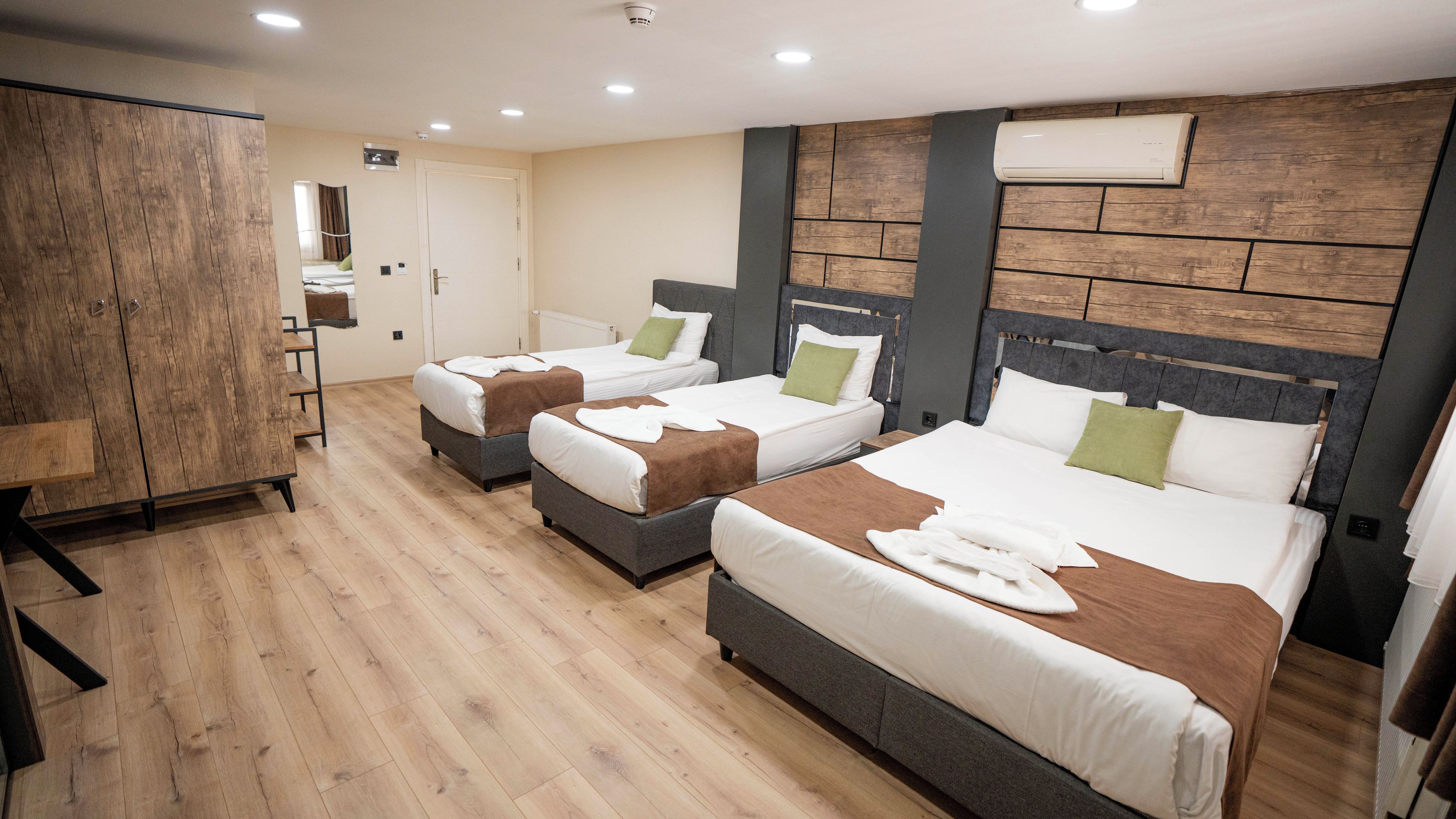 A hotel room with three beds, wooden flooring, a wardrobe, and a mirror.