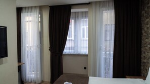 A hotel room with a bed, a TV, a window with curtains, and a view of the outside. - Mila Suites Taksim (Istanbul)