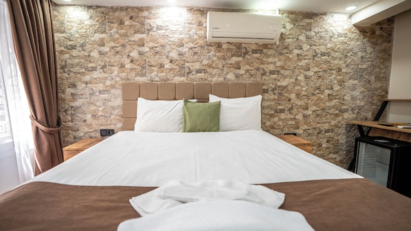 A hotel room with a stone wall, a bed with white bedding, a brown headboard, and a mounted air conditioner. - Mila Suites Taksim (Istanbul)