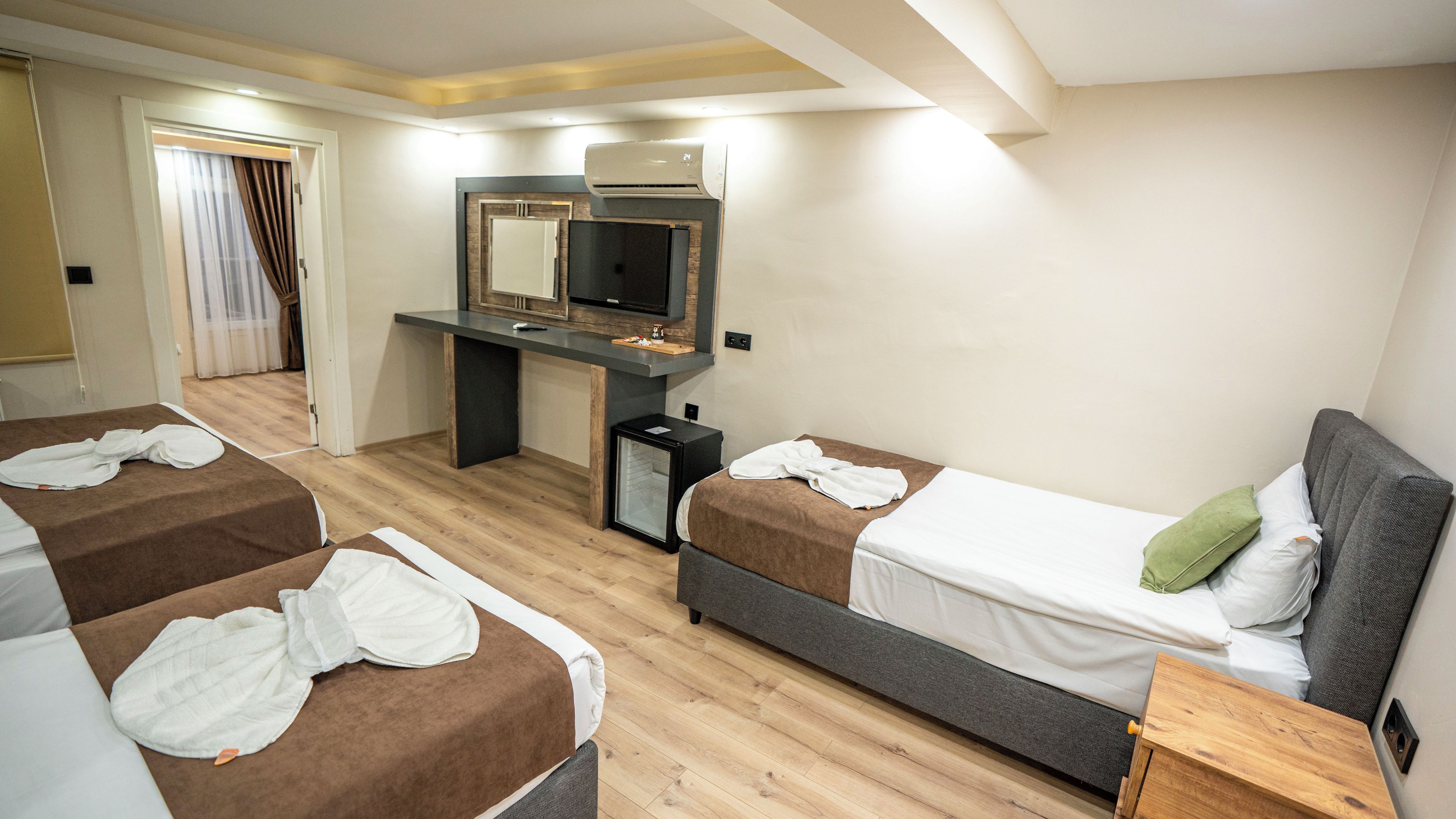 A hotel room with two beds, a desk, a mirror, and a small refrigerator.