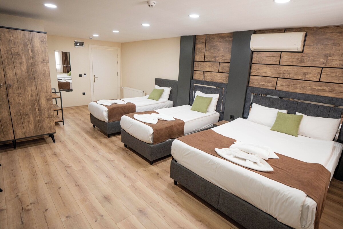 A hotel room with three beds, wooden flooring, a wardrobe, and a mirror.