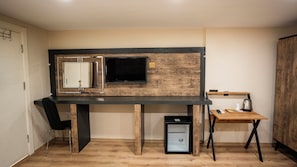 A compact room with a desk, chair, TV, and a small kitchenette area.