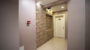 A hallway with a stone wall, a white door labeled '302', and a red emergency box on the wall. - Mila Suites Taksim (Istanbul)