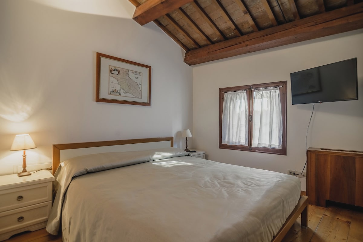 Une chambre à coucher avec un lit, des tables de chevet, une carte accrochée au mur, une fenêtre avec des rideaux et un téléviseur fixé au mur.