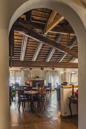 An interior with a wooden ceiling, a dining area with a table and chairs, and a kitchen area with a counter and cabinets. - Le Camere di Palazzo Bortolan (Treviso)