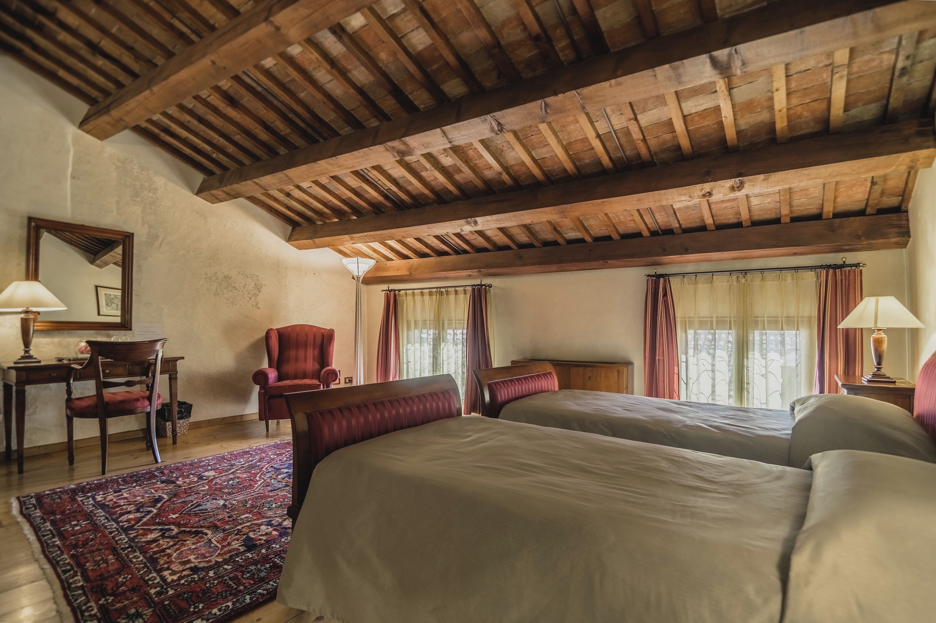 Una habitación con techo de madera, dos camas, una silla, un escritorio y una alfombra.