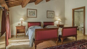 Quarto com teto de madeira, duas camas com cabeceiras vermelhas, abajures, mesa de cabeceira de madeira, cortina listrada em vermelho e branco, e tapete estampado.