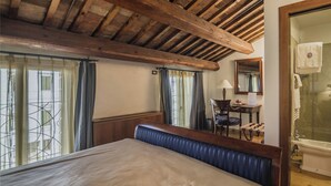 Quarto com teto de madeira, cama com cabeceira azul, escrivaninha com cadeira, espelho e banheiro com banheira.