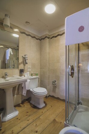 Une salle de bain avec un plancher en bois, un lavabo blanc, des toilettes, une cabine de douche en verre et un miroir.